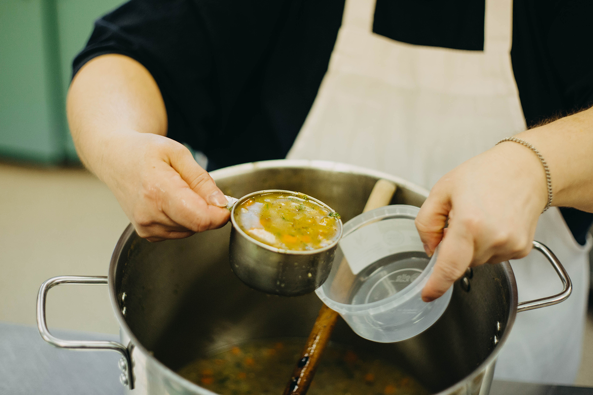 Staff member putting soup from pot into container.