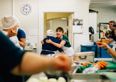 Raw Carrot members hugging and cooking together in soup Kitchen