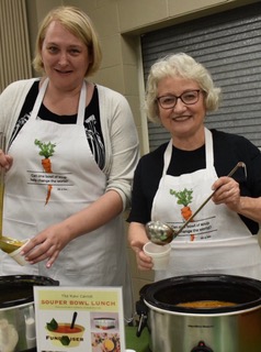 2 ladies wearing aprons serving soup