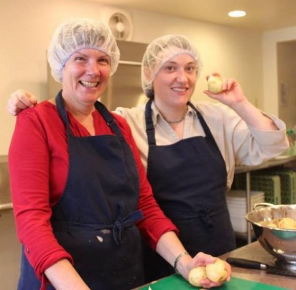 2 smiling ladies in the kitchen prepping onions